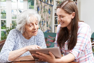 A teen volunteer helping an older woman use a tablet